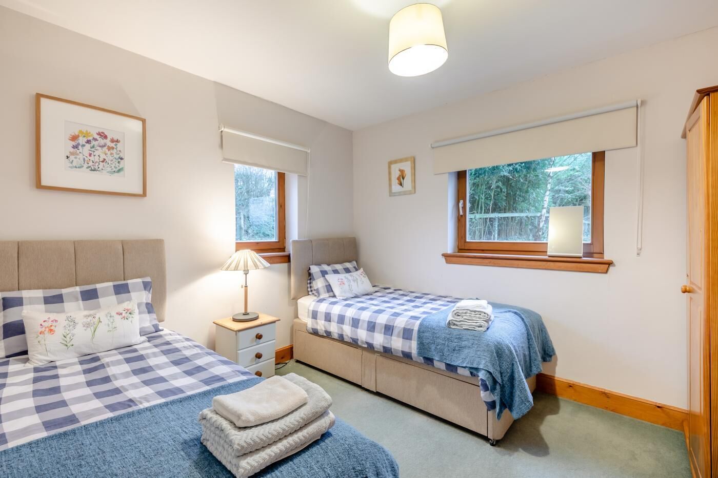 Une chambre avec deux lits, une table de chevet, une lampe et une fenêtre donnant sur des arbres.