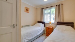 A bedroom with two single beds, a bedside table with a lamp, a radiator, and a window with curtains. - 2 Bed in Mumbles (oc-hh424) (The Mumbles)