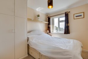 A bedroom with a bed, a window with curtains, a bedside table, and a wall-mounted shelf. - 2 Bed in Mumbles (oc-hh424) (The Mumbles)