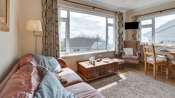 A living room with a leather sofa, a wooden coffee table, a patterned armchair, and a dining area with a table and chairs. - 2 Bed in Mumbles (oc-hh424) (The Mumbles)