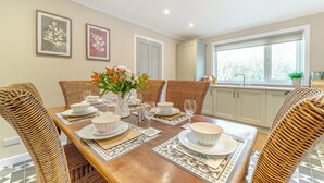 Un comedor con una mesa de madera dispuesta para cuatro personas, rodeado de sillas de mimbre, y un florero con flores sobre la mesa.