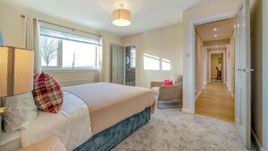 Un dormitorio con una cama, una silla, una lámpara, una ventana y una puerta que da a otra habitación.