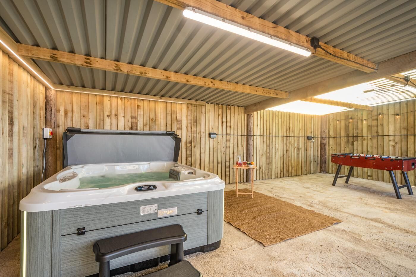 Ein Whirlpool mit Bedienfeld, eine Holzbank und ein Kicker befinden sich in einem Raum mit Holzwänden und einer geneigten Decke.