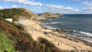 A coastal landscape with rocky terrain, a sandy beach, and a lighthouse. - 1 Bed in Mumbles (oc-hh1205) (The Mumbles)