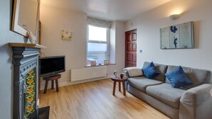 A living room with a fireplace, a television, a sofa, and a window with a view. - 1 Bed in Mumbles (oc-hh1205) (The Mumbles)