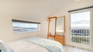 Une chambre à coucher avec un lit, une commode, un miroir et une fenêtre donnant sur la plage.