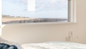 Une chambre dotée d’une grande fenêtre donnant sur une plage, d’un lit et d’une prise électrique fixée au mur.