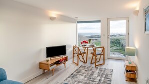 Un salon avec un téléviseur, des meubles en bois, une table à manger avec des chaises, un tapis et une vue sur la mer.