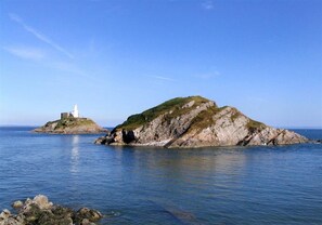 Ein Leuchtturm auf einer felsigen Insel mit ruhigem Wasser und blauem Himmel.