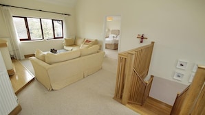 A spacious living room with a large beige sofa, a wooden staircase, and a view through an open door to a bedroom. - 4 Bed in Langland (oc-hh36) (Newton)