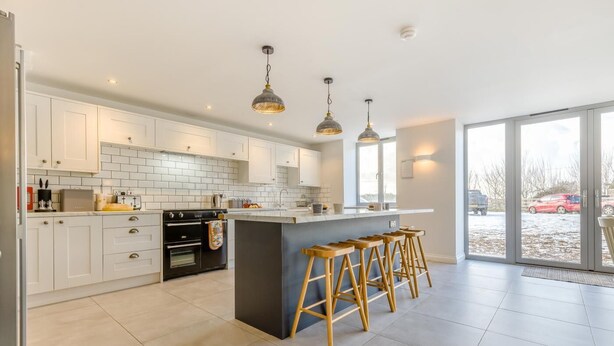 Une cuisine moderne avec des meubles blancs, un îlot central doté de tabourets et un éclairage suspendu.