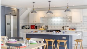 Une cuisine moderne avec des meubles blancs, un îlot central doté de tabourets et un éclairage suspendu.