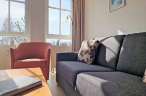 Ein Zimmer mit einer Couch, einem Sessel, einem Tisch und einem Fenster mit Blick.