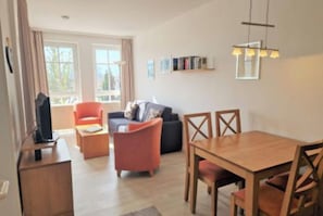 Ein modernes Wohnzimmer mit einer Couch, einem roten Sessel, einem Holzesstzimmer und einem Fernseher.