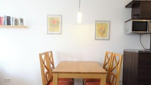 A dining area with a wooden table and chairs, a wall-mounted shelf with books, and a microwave above the cabinets. - Ferienwohnung mit Balkon und Fitnessbereich in Sellin (Sellin)