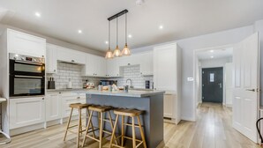 Una cucina moderna con mobili bianchi, forno integrato, isola centrale con sgabelli e illuminazione a sospensione.