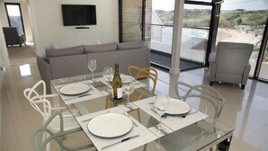 A dining area with a glass table, white plates, and wine glasses, a sofa, and a TV in the background. - 1 Bed in Langland (oc-hh1002) (Newton)