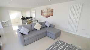 A modern living room with a grey sectional sofa, a patterned rug, and a dining area in the background. - 1 Bed in Langland (oc-hh1002) (Newton)
