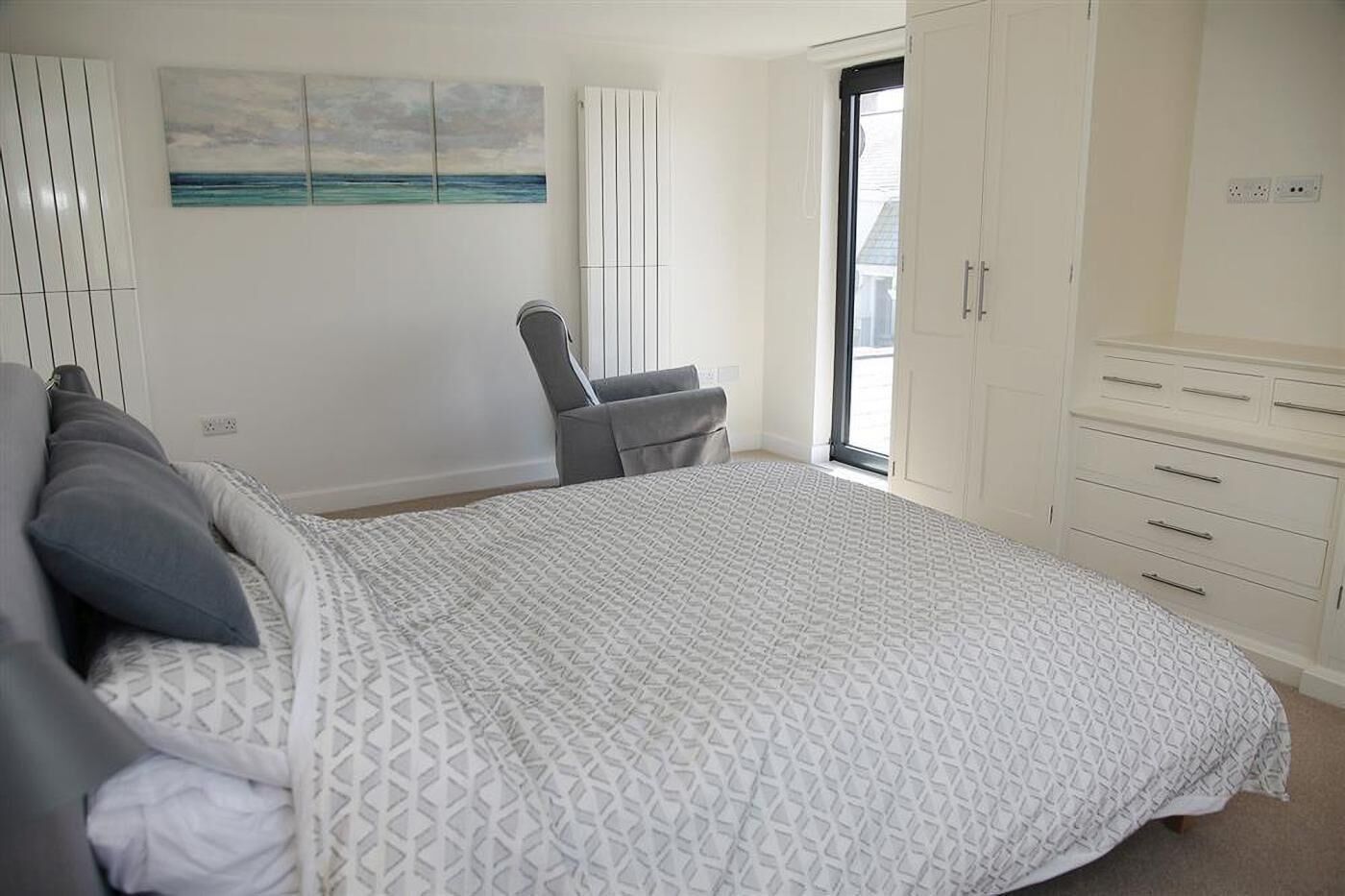 Un dormitorio con cama, una silla, armario y ventana con vistas.