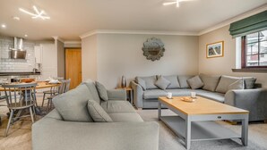 A modern living room with a grey sofa, a wooden coffee table, and a dining area with a table and chairs. - 3 Bed in Dailly (oc-r34760) (Dailly)