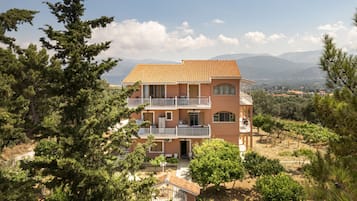 Un edificio a più piani con balconi, circondato da alberi e montagne.