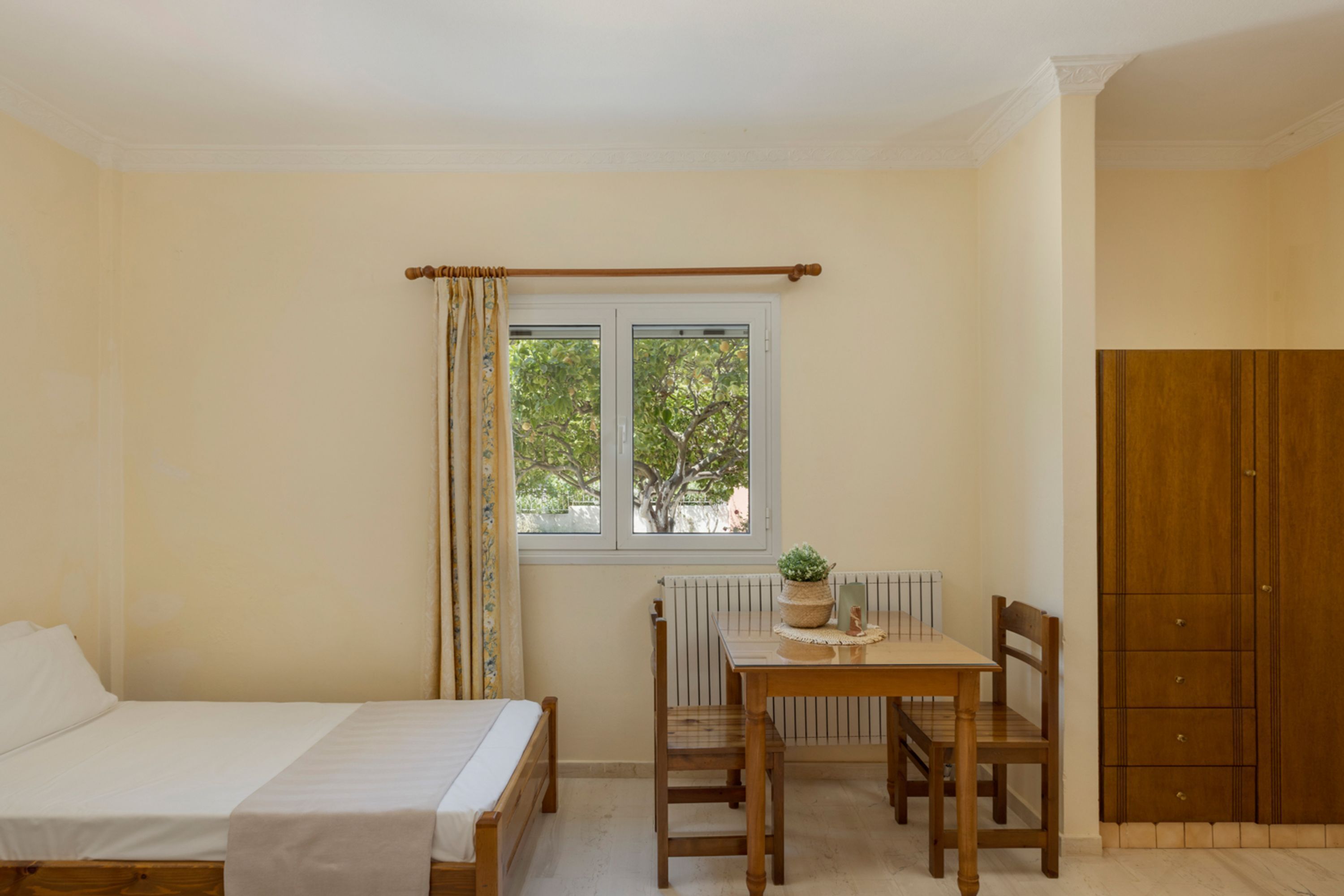 Una camera da letto con un letto, un tavolo con sedie, una finestra con tende e un armadio.