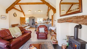 A spacious living room with a leather sofa, a fireplace, and a kitchen in the background. - 3 Bed in Llanrwst (oc-bow155) (Llanrwst)