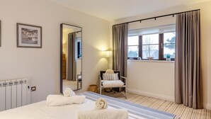 Een hotelkamer met een bed, een stoel, een spiegel, een raam met gordijnen en een radiator.