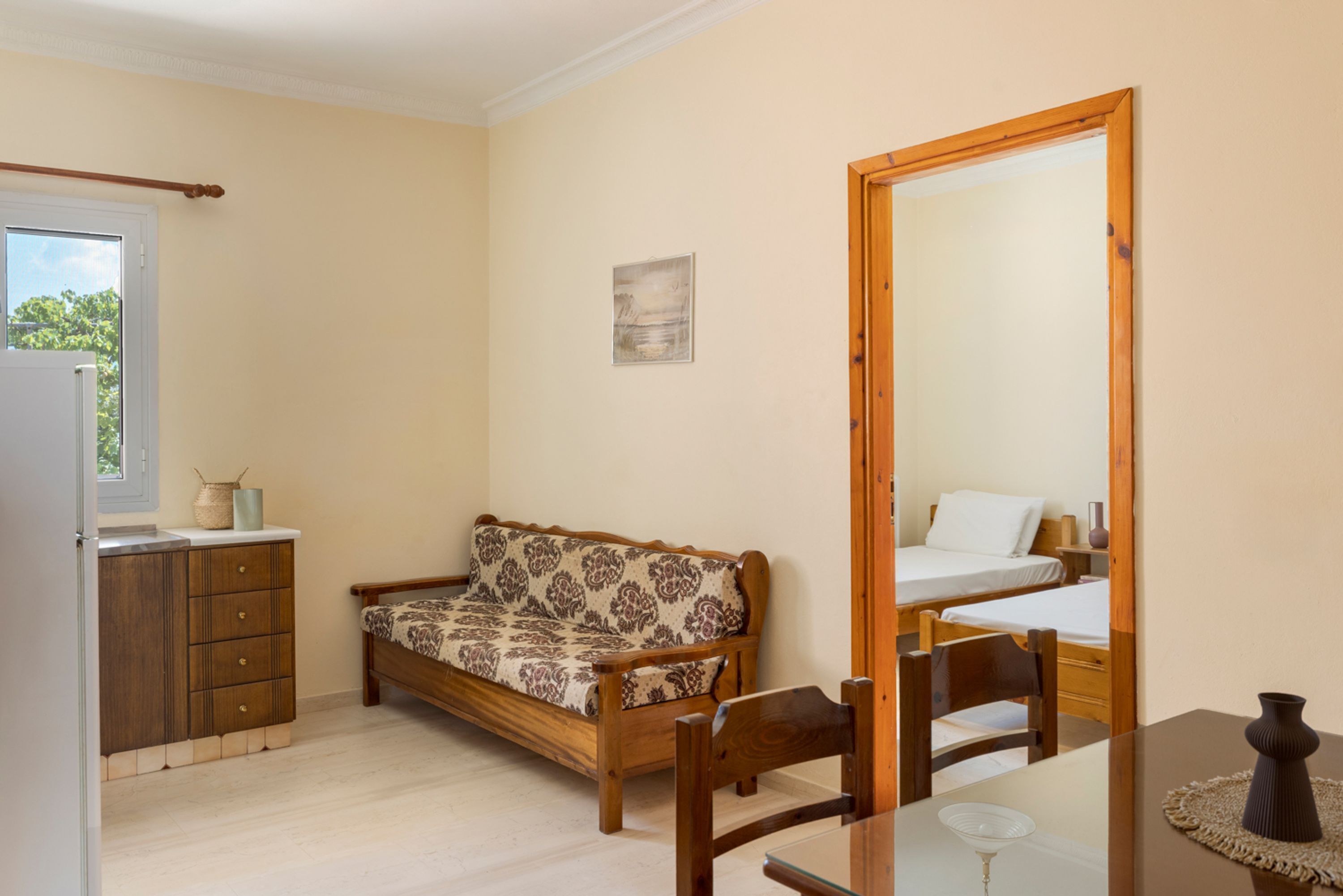 A room with a wooden sofa, a dining table with chairs, a bed, a wooden cabinet, and a mirror.