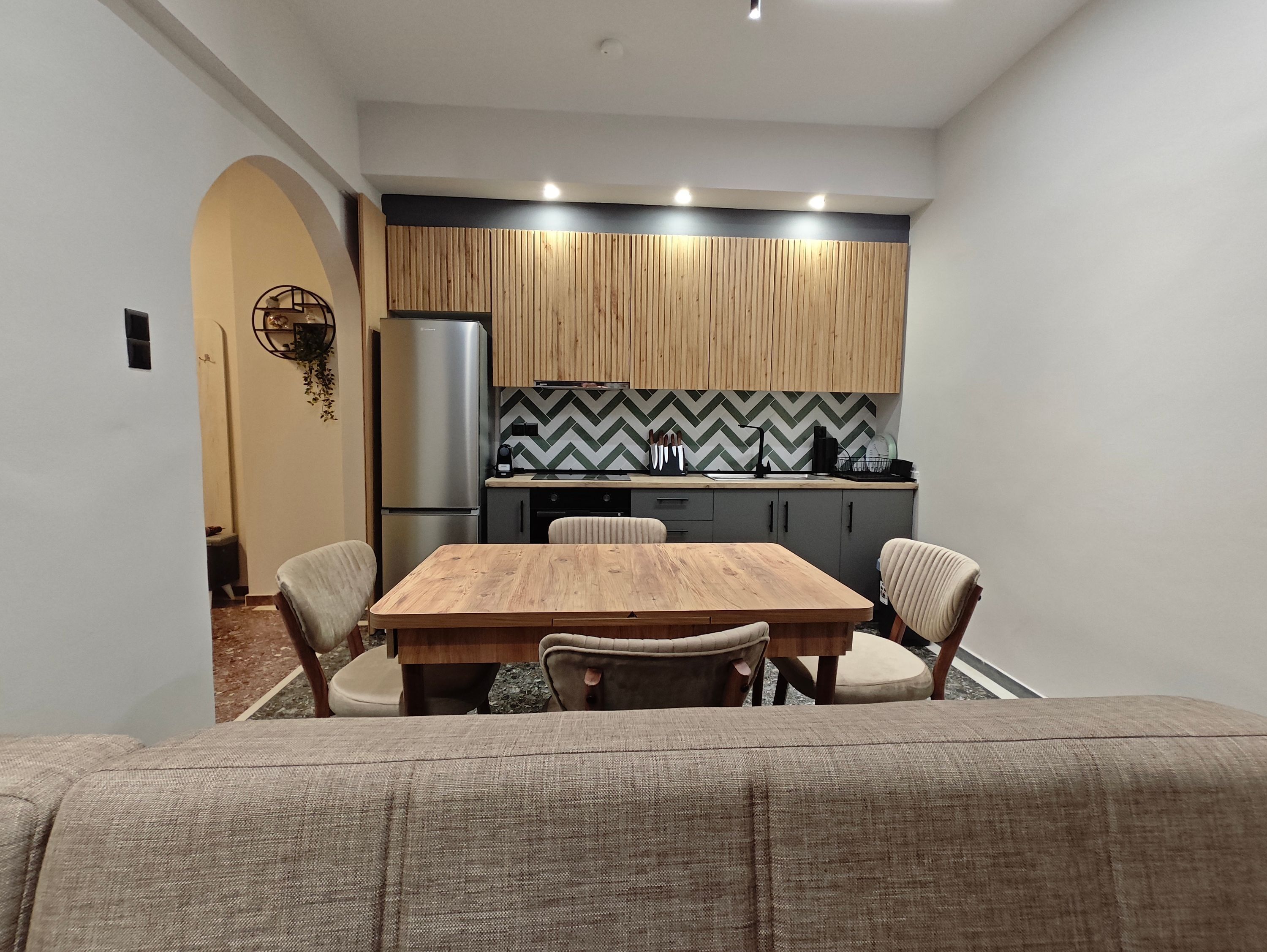 A modern kitchen with a wooden table and chairs, a refrigerator, and a herringbone-patterned backsplash.