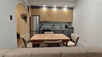 A modern kitchen with a wooden table and chairs, a refrigerator, and a herringbone-patterned backsplash.