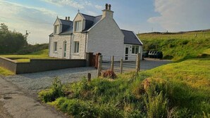 A two-story stone house with a gravel driveway and a fenced area. - 3 Bed in Snizort (oc-h34778) (Snizort)