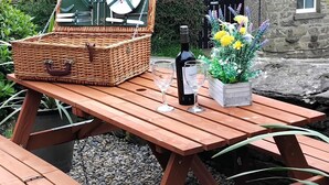 Ein Picknick mit einem Korb aus Weidengeflecht, einer Weinflasche, Gläsern und einer Blumenkomposition auf einem Holztisch.