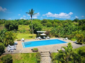 Ein Swimmingpool mit Liegestühlen, umgeben von üppiger Vegetation und blauem Himmel.