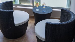 Ein Balkon mit Korbstühlen und einem kleinen Tisch, mit Blick auf einen Kurort mit Gebäuden und Palmen.