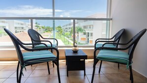 Ein Balkon mit Korbstühlen und einem kleinen Tisch, der auf einen Wohnbereich mit Gebäuden und Grünflächen blickt.