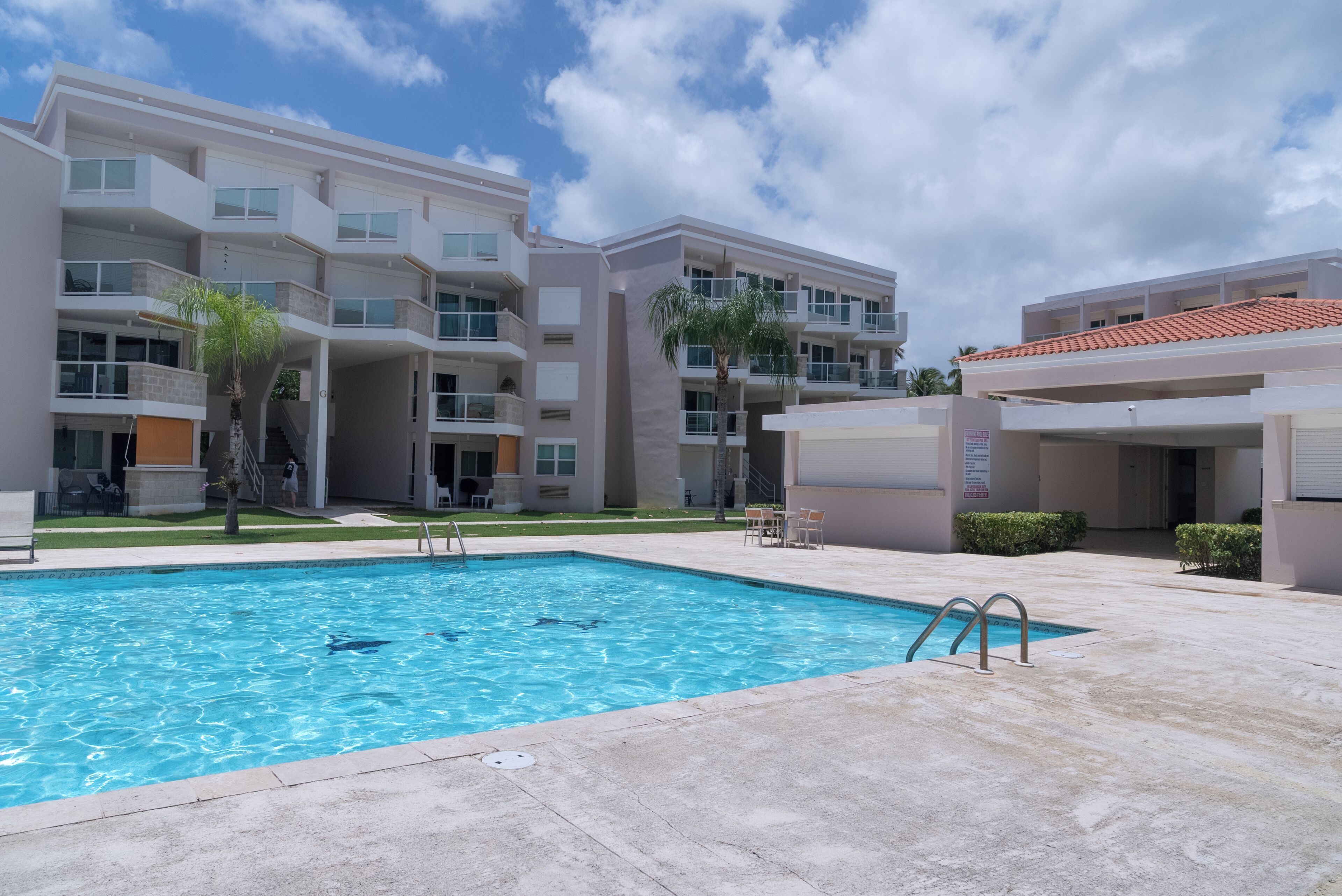 A swimming pool with a clear blue water, surrounded by a building with multiple balconies and a tiled roof.