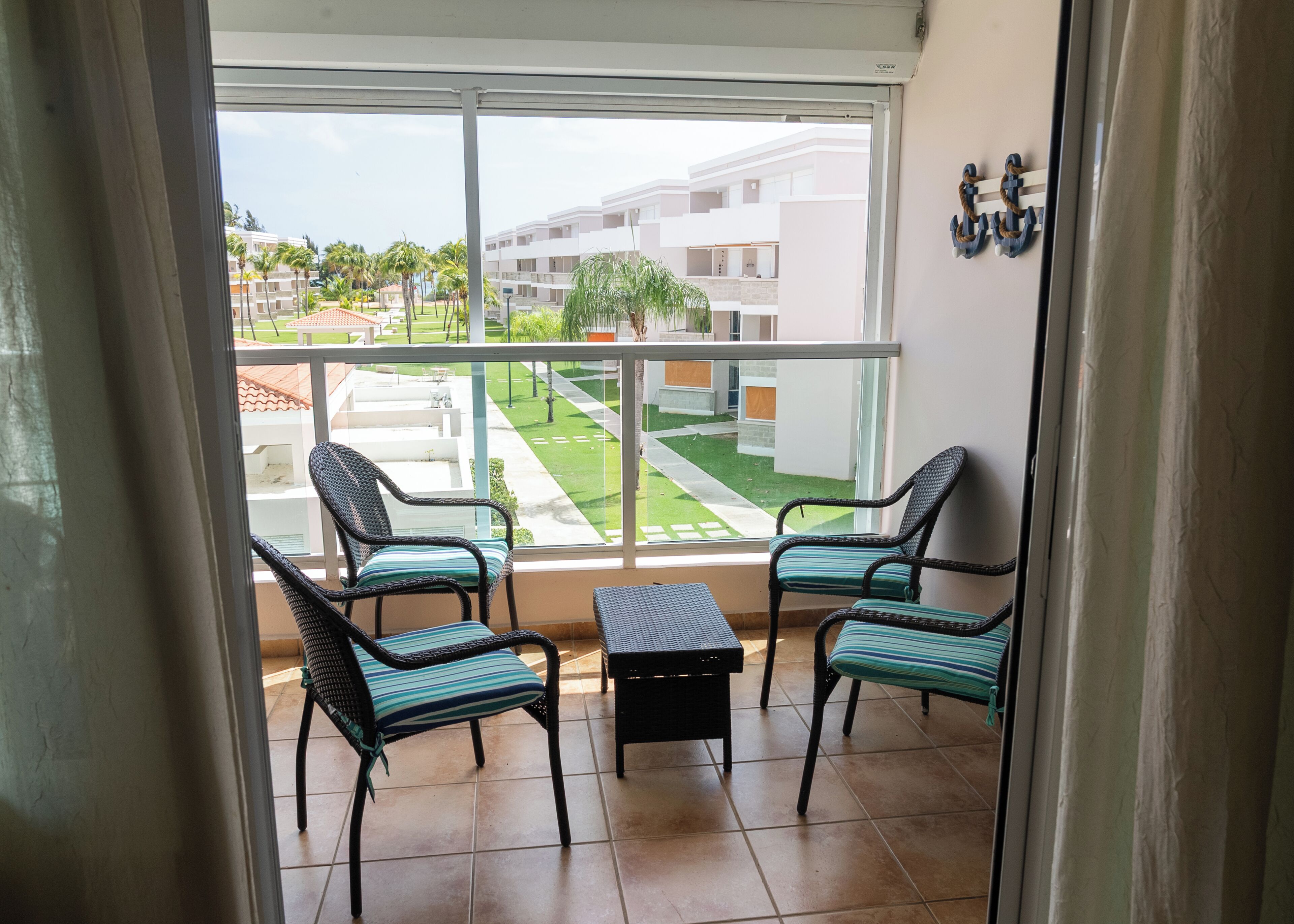 Een balkon met rieten stoelen en een kleine tafel, met uitzicht op een verzorgd gazon en gebouwen.