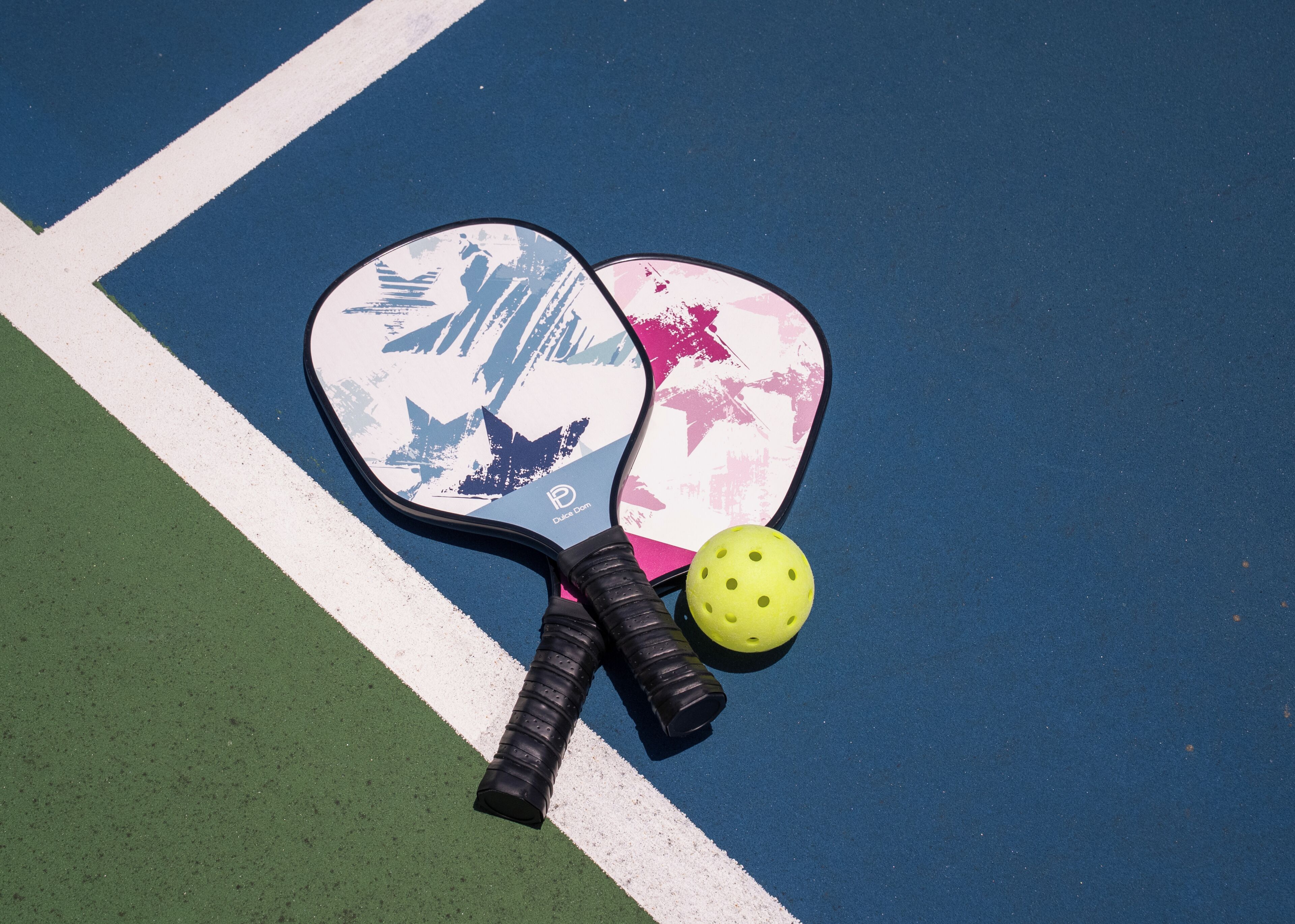 Two paddleball paddles and a ball on a blue court with white lines.