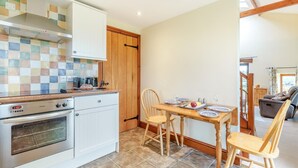 Een keuken met een fornuis, oven en een betegelde spatwand, een eettafel met stoelen en uitzicht op de woonkamer.