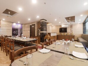 A restaurant with multiple dining tables, chairs, a television, and a fireplace. - Townhouse DJ Grand (Tirupati)