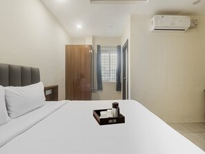 A hotel room with a bed, a wardrobe, a nightstand, a tray with a coffee maker, and an air conditioning unit. - Townhouse DJ Grand (Tirupati)