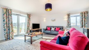 Ein Wohnzimmer mit Sofa, Couchtisch, Fernseher und Blick durch große Fenster.