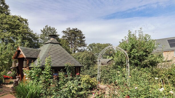 Un jardín con un porche, un arco de madera y diversas plantas.