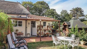 Una casa con techo de paja, un jardín con mesa y sillas de patio, y una variedad de plantas en macetas.