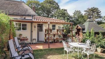 A house with a thatched roof, a garden with a patio table and chairs, and a variety of potted plants.