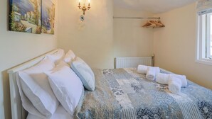 Un dormitorio con cama, almohadas, un radiador, una lámpara de pared, una ventana y un cuadro.