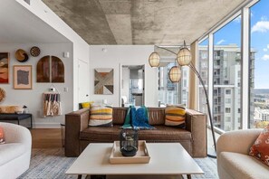 Een moderne woonkamer met een bruine bank, een witte salontafel en een groot raam met uitzicht op de stad.