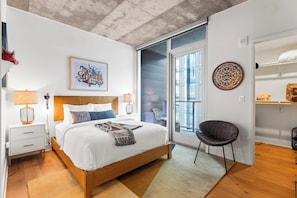 A bedroom with a bed, bedside lamps, a chair, a window, and a door leading to an outdoor area. - 2810 ATX Lux Penthouse | Rooftop Pool, Lake Views & Rainey St Nightlife (Austin)