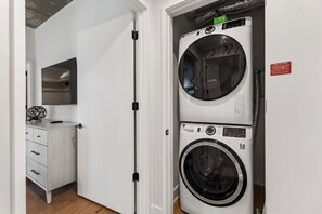 A laundry room with stacked washers and dryers, a white cabinet, and a door. - 2810 ATX Lux Penthouse | Rooftop Pool, Lake Views & Rainey St Nightlife (Austin)